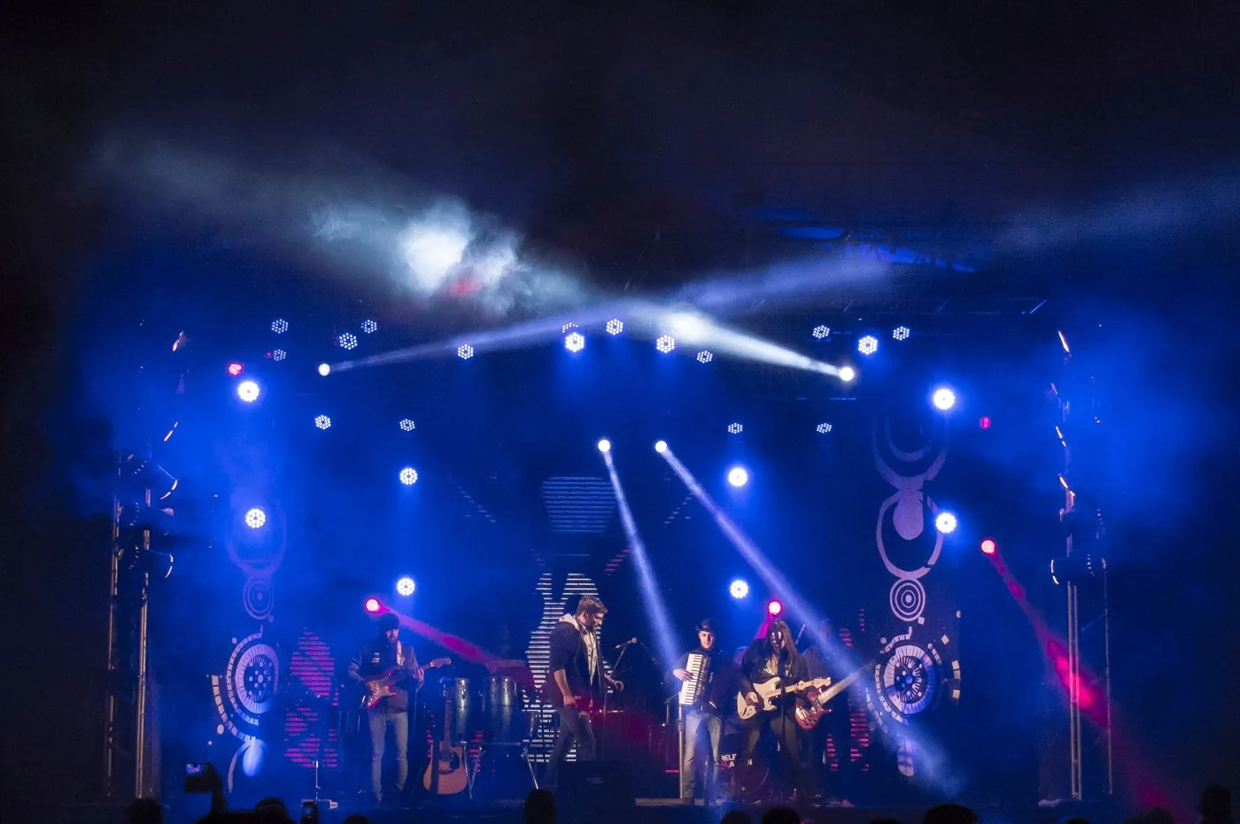Banda en un escenario de festival con iluminación azul y público.